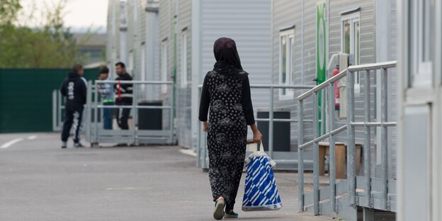 eine Frau mit schwarzem Kopftuch und schwarzem Kleid ist von hinten zu sehen, die geht an weißen Unterkünften für Geflüchtete vorbei eine Frau mit schwarzem Kopftuch und schwarzem Kleid ist von hinten zu sehen, die geht an weißen Unterkünften für Geflüchtete vorbei