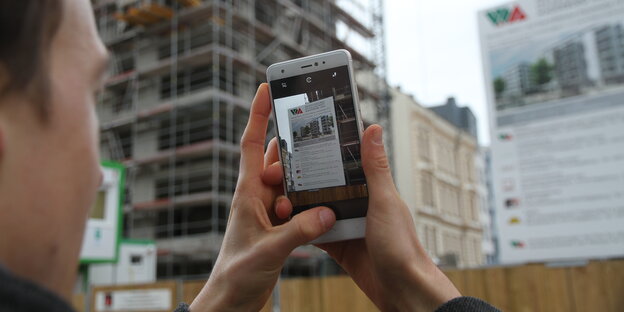Ein Mann guckt auf ein Smartphone-Bildschirm. Er fotografiert eine Werbetafel Ein Mann guckt auf ein Smartphone-Bildschirm. Er fotografiert eine Werbetafel