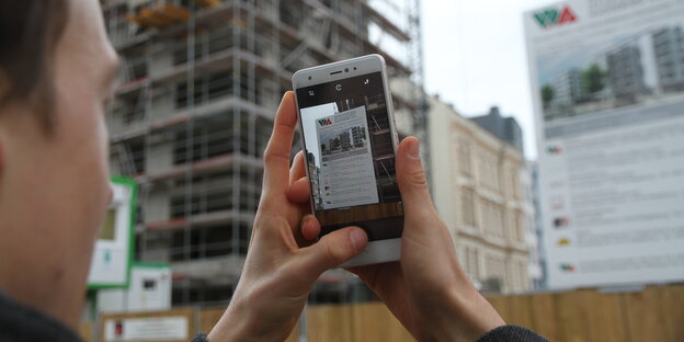 Ein Mann guckt auf ein Smartphone-Bildschirm. Er fotografiert eine Werbetafel