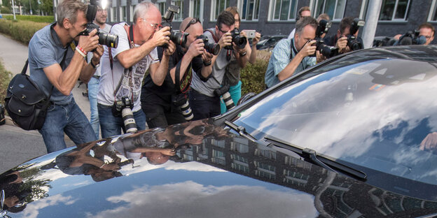 Eine Medienmeute beugt sich gierig über ein schwarzes Auto Eine Medienmeute beugt sich gierig über ein schwarzes Auto