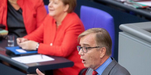 Dietmar Bartsch spricht im Bundestag, im Hintergrund sitzt Angela Merkel Dietmar Bartsch spricht im Bundestag, im Hintergrund sitzt Angela Merkel
