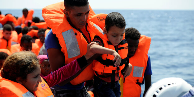 Ein Mann hebt einen kleinen Jungen in Rettungsweste auf ein Schiff Ein Mann hebt einen kleinen Jungen in Rettungsweste auf ein Schiff