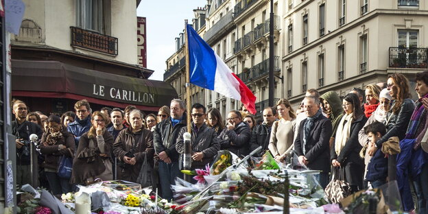 Menschen stehen vor dem Pariser Café Le Carillon, vor ihnen auf dem Boden haben Menschen Kerzen und Blumen abgelegt Menschen stehen vor dem Pariser Café Le Carillon, vor ihnen auf dem Boden haben Menschen Kerzen und Blumen abgelegt