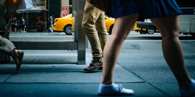 Eine Straßenszene, hinten sind beigebehoste Männerbeine zu sehen, vorne nackte Frauenbeine unter einem Rock Eine Straßenszene, hinten sind beigebehoste Männerbeine zu sehen, vorne nackte Frauenbeine unter einem Rock