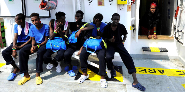 Sechs Männer, gerettete Flüchtlinge, sitzen an Bord eines Schiffes Sechs Männer, gerettete Flüchtlinge, sitzen an Bord eines Schiffes