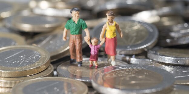 Zwei Erwachsene und ein Kind als Spielfiguren. Sie gehen gemeinsam Hand-in-Hand über einen Haufen mit Euromünzen Zwei Erwachsene und ein Kind als Spielfiguren. Sie gehen gemeinsam Hand-in-Hand über einen Haufen mit Euromünzen