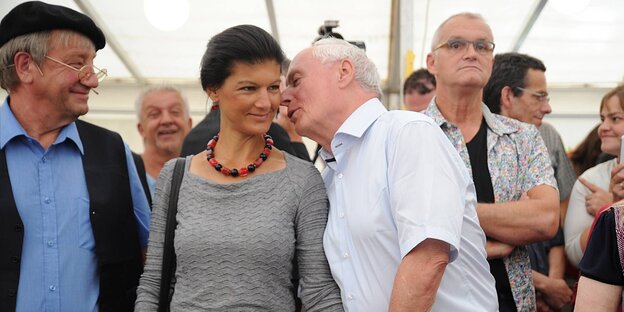 Oskar Lafontaine flüstert Sahra Wagenknecht etwas ins Ohr, während sie von vielen Menschen in einem Bierzelt umgeben sind