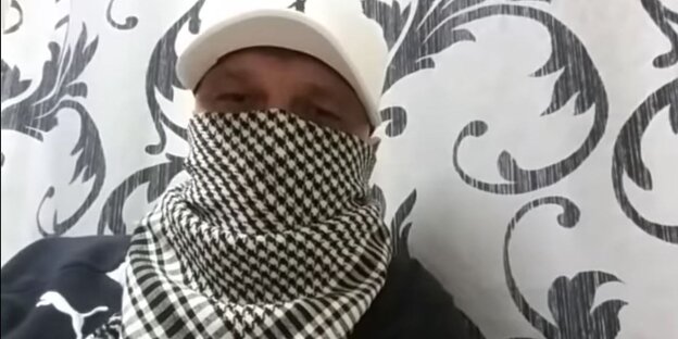 Der inhaftierte YouTuber vor einer Wand. Er trägt eine Kappe und ein Tuch, um sein Gesicht zu verschleiern. Der inhaftierte YouTuber vor einer Wand. Er trägt eine Kappe und ein Tuch, um sein Gesicht zu verschleiern.
