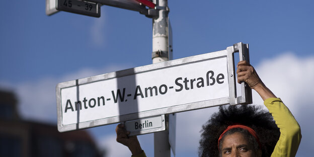 Eine Frau hält ein Straßenschild mit den Namen Anton-W.-Amo-Straße hoch Eine Frau hält ein Straßenschild mit den Namen Anton-W.-Amo-Straße hoch