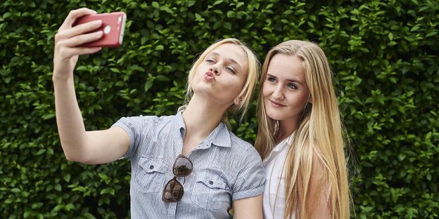 Verschwommen und grau wird ein Handy gezeigt, mit dem zwei Personen ein Selfie schießen Verschwommen und grau wird ein Handy gezeigt, mit dem zwei Personen ein Selfie schießen