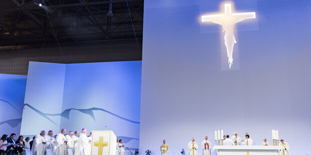 Katholische Würdenträger vor einer blau erleuchteten Wand mit einem strahlenden Riesenkreuz Katholische Würdenträger vor einer blau erleuchteten Wand mit einem strahlenden Riesenkreuz