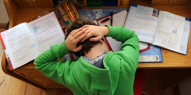 Ein Kind hat den Kopf zwischen seine Schulbücher auf den Tisch gelegt und die Hände im Nacken gefaltet. Ein Kind hat den Kopf zwischen seine Schulbücher auf den Tisch gelegt und die Hände im Nacken gefaltet.