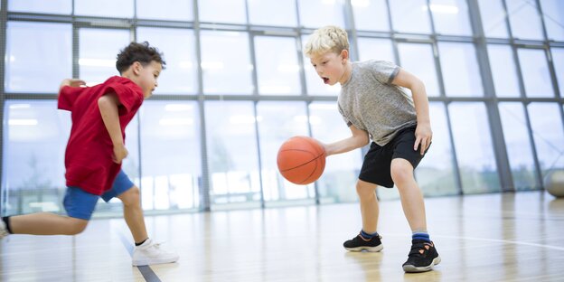 Zwei Jungen beim Dribbeln mit dem Basketball in der Halle Zwei Jungen beim Dribbeln mit dem Basketball in der Halle