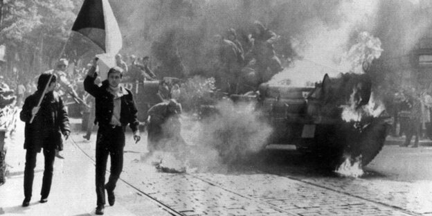 Demonstranten gehen am 21.08.1968 in Prag mit der tschechischen Flagge neben einem brennenden sowjetischen Panzer