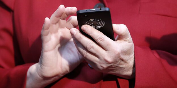 Angela Merkel hält ein Smartphone mit Bundesadler in der Hand Angela Merkel hält ein Smartphone mit Bundesadler in der Hand
