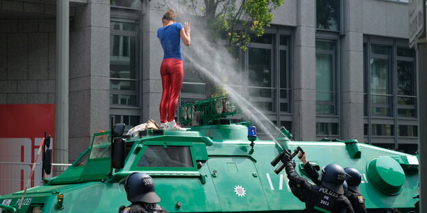 Zwei Polizisten sprühen mit Pfefferspray auf eine Demonstrantin, die auf einem Polizeipanzer steht Zwei Polizisten sprühen mit Pfefferspray auf eine Demonstrantin, die auf einem Polizeipanzer steht