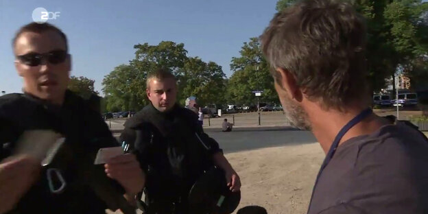 Zwei Polizisten und ein Mann stehen sich gegenüber Zwei Polizisten und ein Mann stehen sich gegenüber