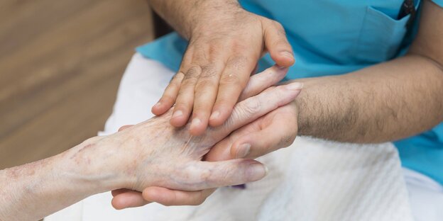 Die beiden Hände eines jüngeren Mannes berühren die Hand eines älteren Menschen Die beiden Hände eines jüngeren Mannes berühren die Hand eines älteren Menschen