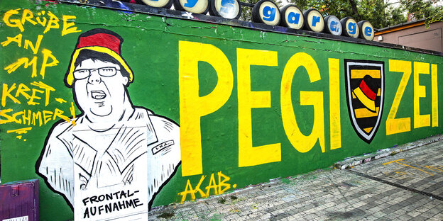 Eine grün gestrichene Wand, darauf der Schriftzug „Pegizei“ und das Abbild des sogenannten „Hutbürgers“, der sich über ein ZDF-Fernsehteam beschwert hatte Eine grün gestrichene Wand, darauf der Schriftzug „Pegizei“ und das Abbild des sogenannten „Hutbürgers“, der sich über ein ZDF-Fernsehteam beschwert hatte