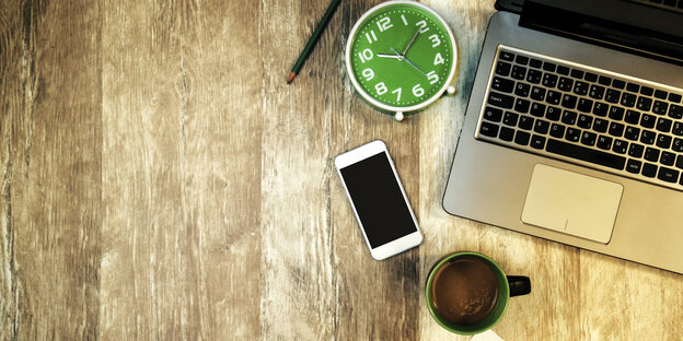 Ein Schreibtisch, darauf ein Smartphone, ein Computer, ein Wecker und eine Kaffeetasse Ein Schreibtisch, darauf ein Smartphone, ein Computer, ein Wecker und eine Kaffeetasse