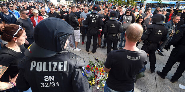 Blumen liegen auf dem Boden, daneben stehen Polizisten und BürgerInnen