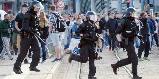 Polizisten laufen durch die Stadt, dahinter Passanten Polizisten laufen durch die Stadt, dahinter Passanten