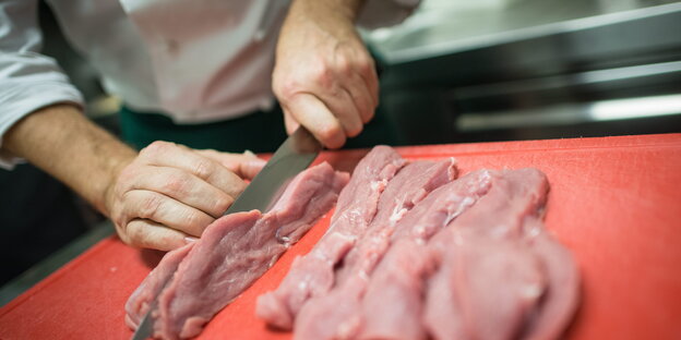 Jemand steht hinter einem roten Brett, auf dem drei Stücke Fleisch liegen Jemand steht hinter einem roten Brett, auf dem drei Stücke Fleisch liegen