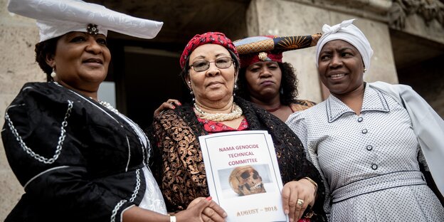 Herero- und Nama-Aktivistinnen stehen nebeneinander und halten ein Report Herero- und Nama-Aktivistinnen stehen nebeneinander und halten ein Report