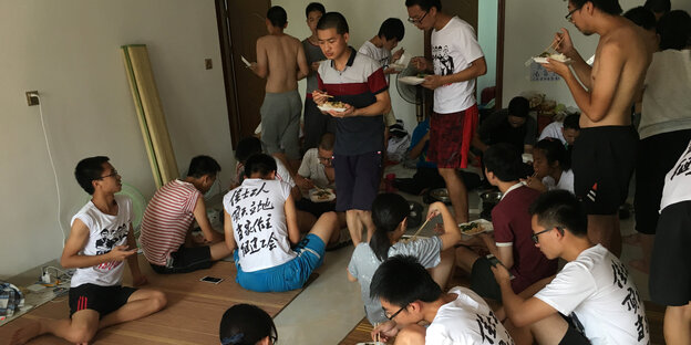 Eine Grupper junger Chinesen isst gemeinsam, teils auf dem Boden sitzend, manche tragen dasselbe Tshirt Eine Grupper junger Chinesen isst gemeinsam, teils auf dem Boden sitzend, manche tragen dasselbe Tshirt