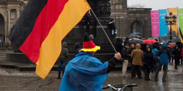 Bei Pegida in Dresden steht ein Mann mit Deutschlandhut und Deutschlandfahne Bei Pegida in Dresden steht ein Mann mit Deutschlandhut und Deutschlandfahne
