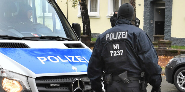 Vermummter Polizist neben einem Polizeiwagen Vermummter Polizist neben einem Polizeiwagen