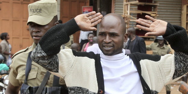 In Uganda führt ein uniformierter Mann einen Mann mit erhobenen Händen ab In Uganda führt ein uniformierter Mann einen Mann mit erhobenen Händen ab