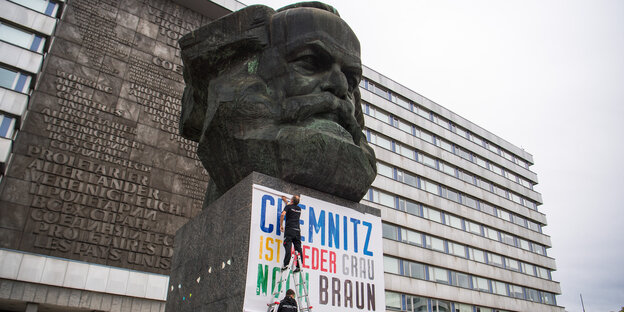 Zwei Männer befestigen am Karl-Marx-Denkmal ein Plakat mit der Aufschrift "Chemnitz ist weder grau noch braun". Zwei Männer befestigen am Karl-Marx-Denkmal ein Plakat mit der Aufschrift "Chemnitz ist weder grau noch braun".