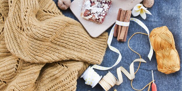 Ein Strickpullover liegt neben einem Stück Streuselkuchen und mehreren Bastelmaterialien Ein Strickpullover liegt neben einem Stück Streuselkuchen und mehreren Bastelmaterialien