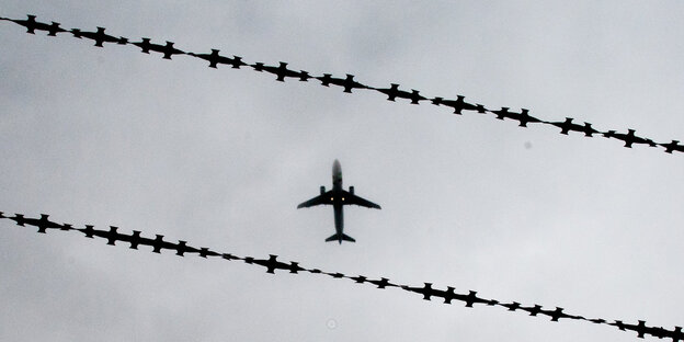 Ein fliegendes Flugzeug am Himmel zwischen Stacheldraht