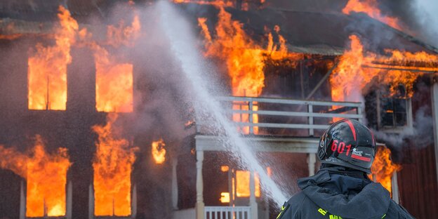 Ein Feuerwehrmann löscht ein brennendes Haus Ein Feuerwehrmann löscht ein brennendes Haus
