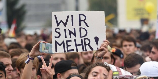 Köpfe von einer Menge Demonstranten. Aus der Menge heraus ragt ein Schild mit der Aufschrift „Wir sind mehr“ Köpfe von einer Menge Demonstranten. Aus der Menge heraus ragt ein Schild mit der Aufschrift „Wir sind mehr“
