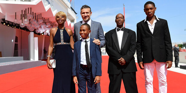 Auf einem roten Teppich stehen Judy Hill, Roberto Minervini, Kevin Goodman und Ronaldo King, im Vordergrnd Titus Turner Auf einem roten Teppich stehen Judy Hill, Roberto Minervini, Kevin Goodman und Ronaldo King, im Vordergrnd Titus Turner