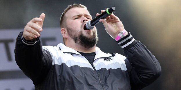 Sänger von Feine Sahne Fischfilet beim Singen mit Mikro auf der Bühne Sänger von Feine Sahne Fischfilet beim Singen mit Mikro auf der Bühne