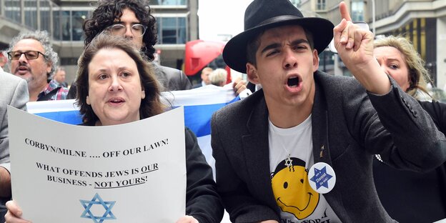 Eine Frau hält ein Schild gegen Antisemitismus hoch, das sich an die Parteiführung richtet, ein Mann daneben trägt eine Davidsternkette Eine Frau hält ein Schild gegen Antisemitismus hoch, das sich an die Parteiführung richtet, ein Mann daneben trägt eine Davidsternkette