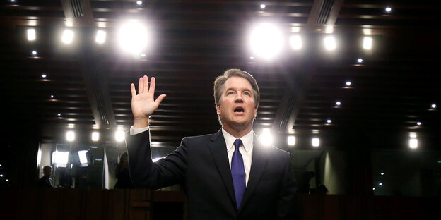 Brett Kavanaugh hebt seine linke Hand zur Vereidigung, hinter ihm Blitzlichter Brett Kavanaugh hebt seine linke Hand zur Vereidigung, hinter ihm Blitzlichter