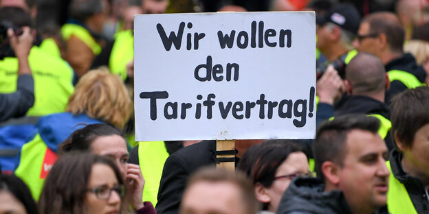 Demonstranten halten ein Schild hoch, auf dem steht: "Wir wollen den Tarifvertrag". Demonstranten halten ein Schild hoch, auf dem steht: "Wir wollen den Tarifvertrag".
