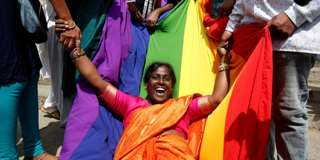 Eine Frau liegt glücklich auf einer Regenbogenflagge und wird von anderen Personen festgehalten Eine Frau liegt glücklich auf einer Regenbogenflagge und wird von anderen Personen festgehalten