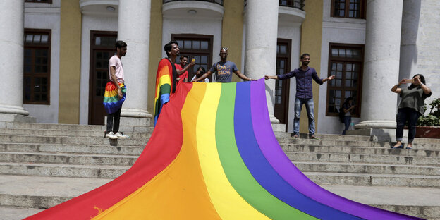 Vor einem Gebäude wird von mehreren Personen eine riesige Regenbogenfahne ausgerollt