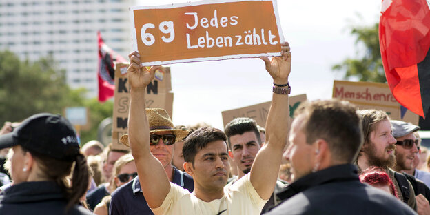 Ein Mann hält auf einer Demo ein Schild hoch, darauf steht "69 – jedes Leben zählt"