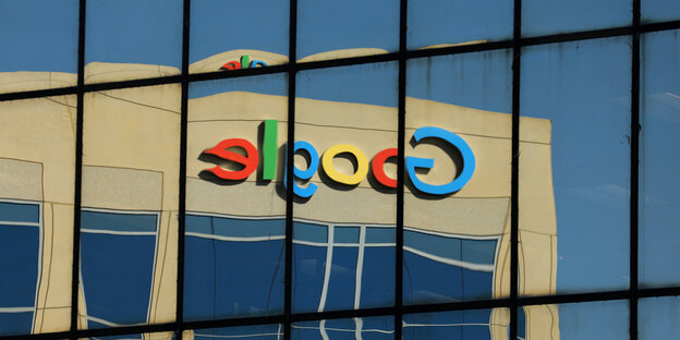 Ein Google-Logo, das an einer Fassade angebracht ist, spiegelt sich in einer Glasfassade Ein Google-Logo, das an einer Fassade angebracht ist, spiegelt sich in einer Glasfassade