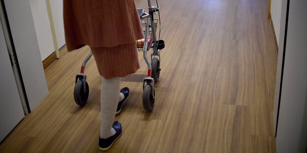Eine Frau mit Rollator geht über einen Flur. Eine Frau mit Rollator geht über einen Flur.