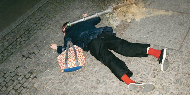 Gestelltes Foto einer Person, die auf dem Gehweg auf dem Bauch liegt, scheinbar von einem Poller erschlagen Gestelltes Foto einer Person, die auf dem Gehweg auf dem Bauch liegt, scheinbar von einem Poller erschlagen