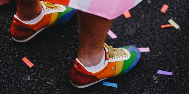 Zwei Regenbogenfarbige Turnschuhe auf grauem Asphalt Zwei Regenbogenfarbige Turnschuhe auf grauem Asphalt