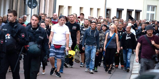 Menschen laufen über eine Straße, flankiert von Polizisten Menschen laufen über eine Straße, flankiert von Polizisten